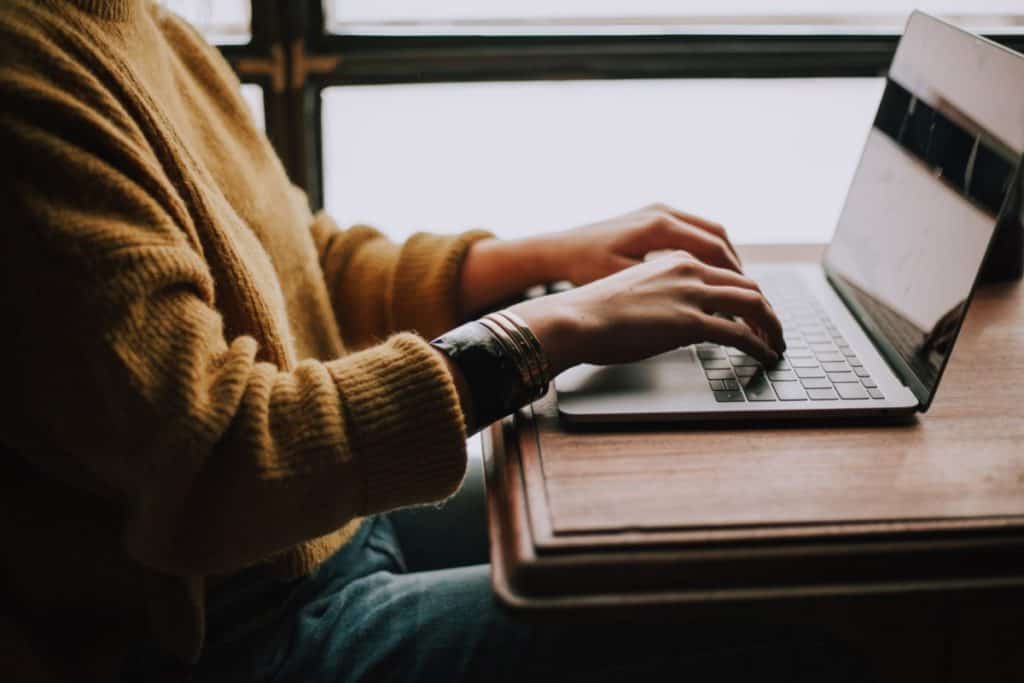 Person in a sweater on their laptop on wooden table