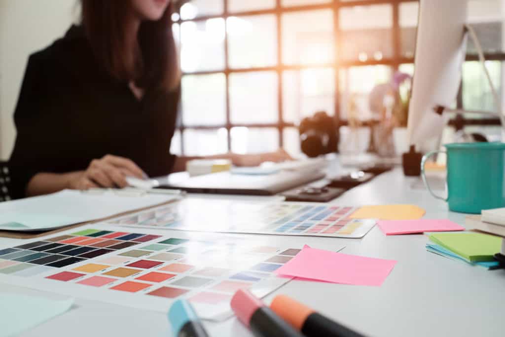 White desk with highlighters, sticky notes, and a folder with somebody sitting at it.