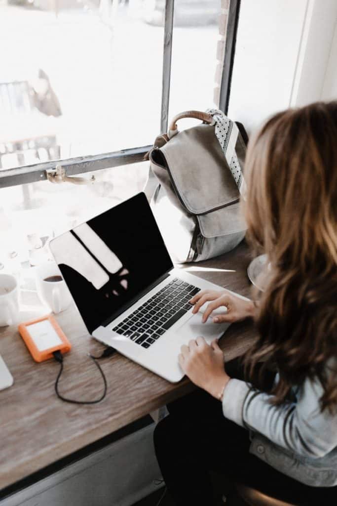 A women sitting at a wooden desk with silver Macbook open