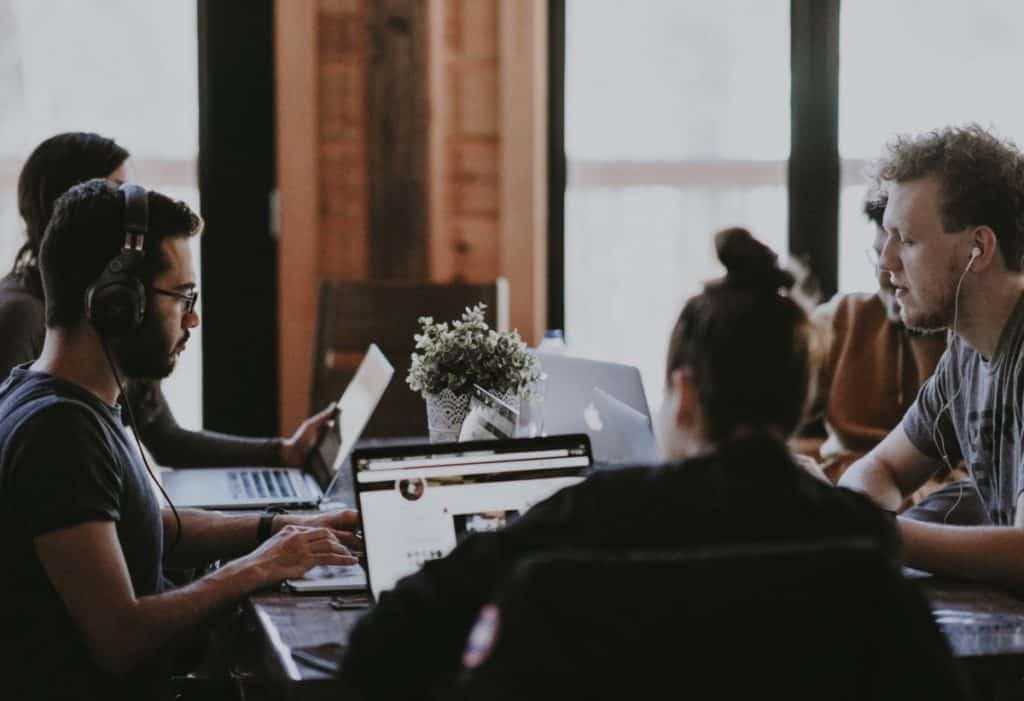 Group of people sitting around a table with laptops open